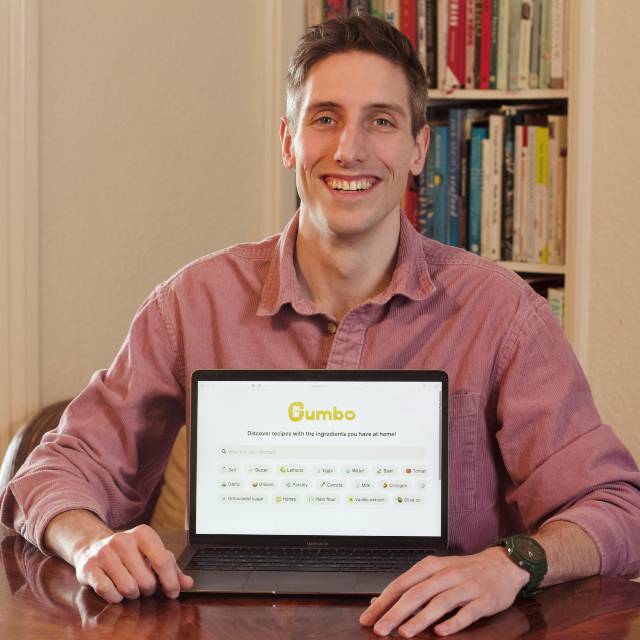 Jacob Strauss smiling behind a a laptop showing Gumbo's landing page.